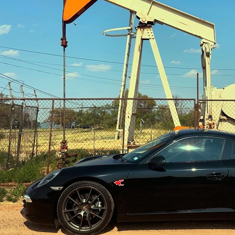 Dillo sticker on a black Porsche 911 in front of an oil pump jack